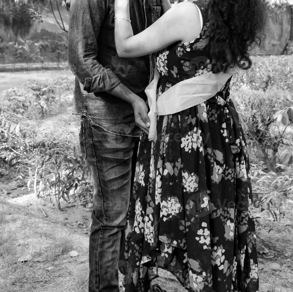 Indian couple posing for maternity baby shoot. The couple is posing in a lawn with green grass and the woman is falunting her baby bump in Lodhi Garden in New Delhi, India - Black and White photo