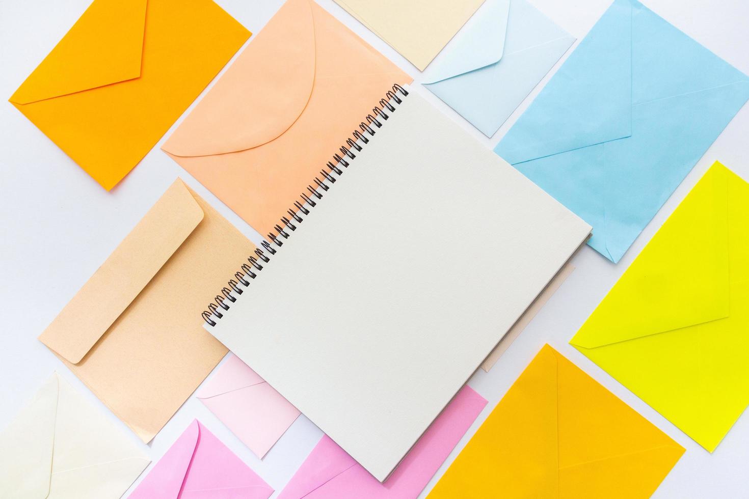 Envelopes in pastel colors align in oblique style with a blank white sketchbook photo