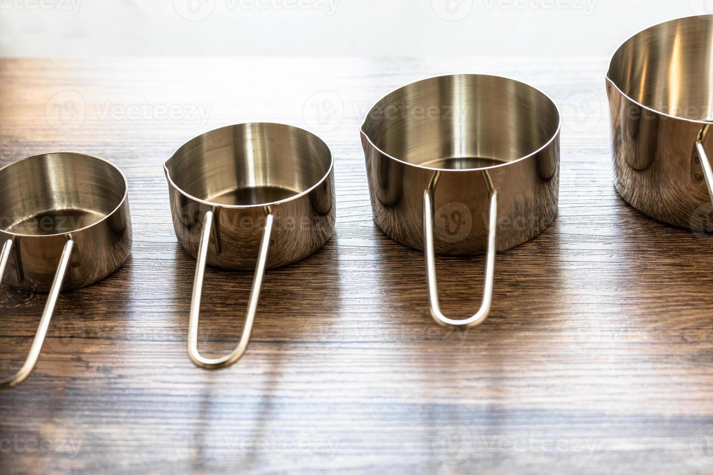 Set of measuring cups made from stainless with a handle on wooden tabletop photo