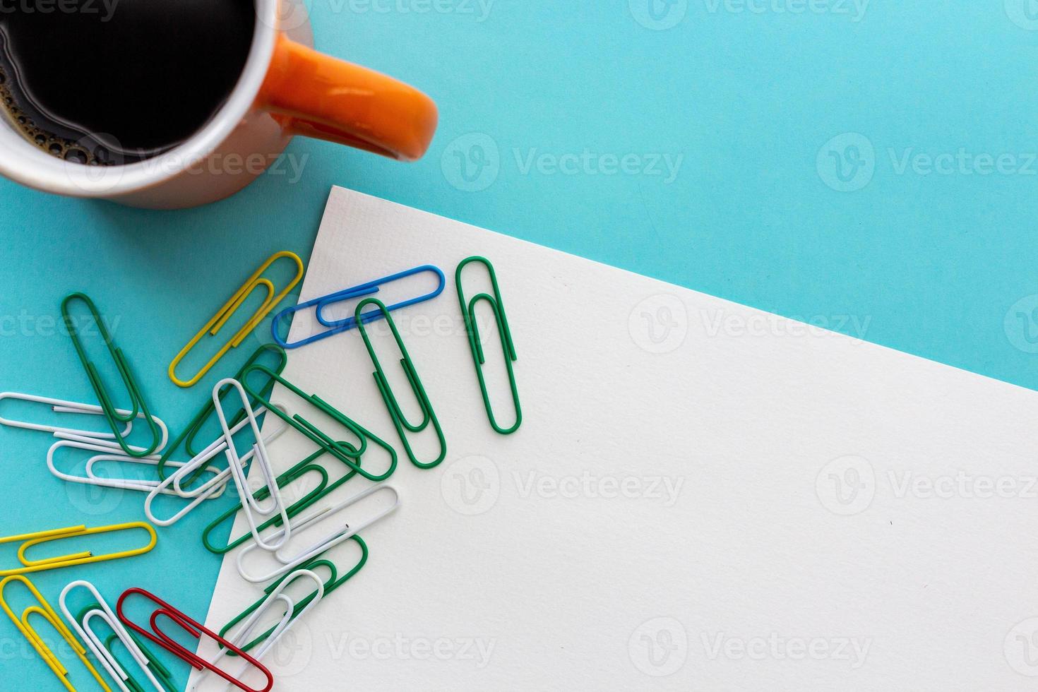 Desktop design with orange mug of coffee and colorful paperclips photo