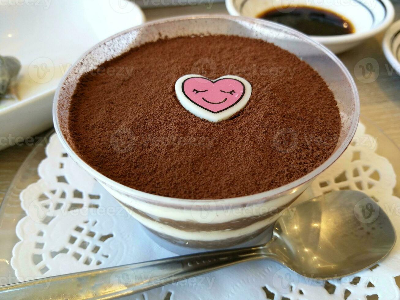 Tiramisu dessert served in a cup and has a cartoon heart on top. photo