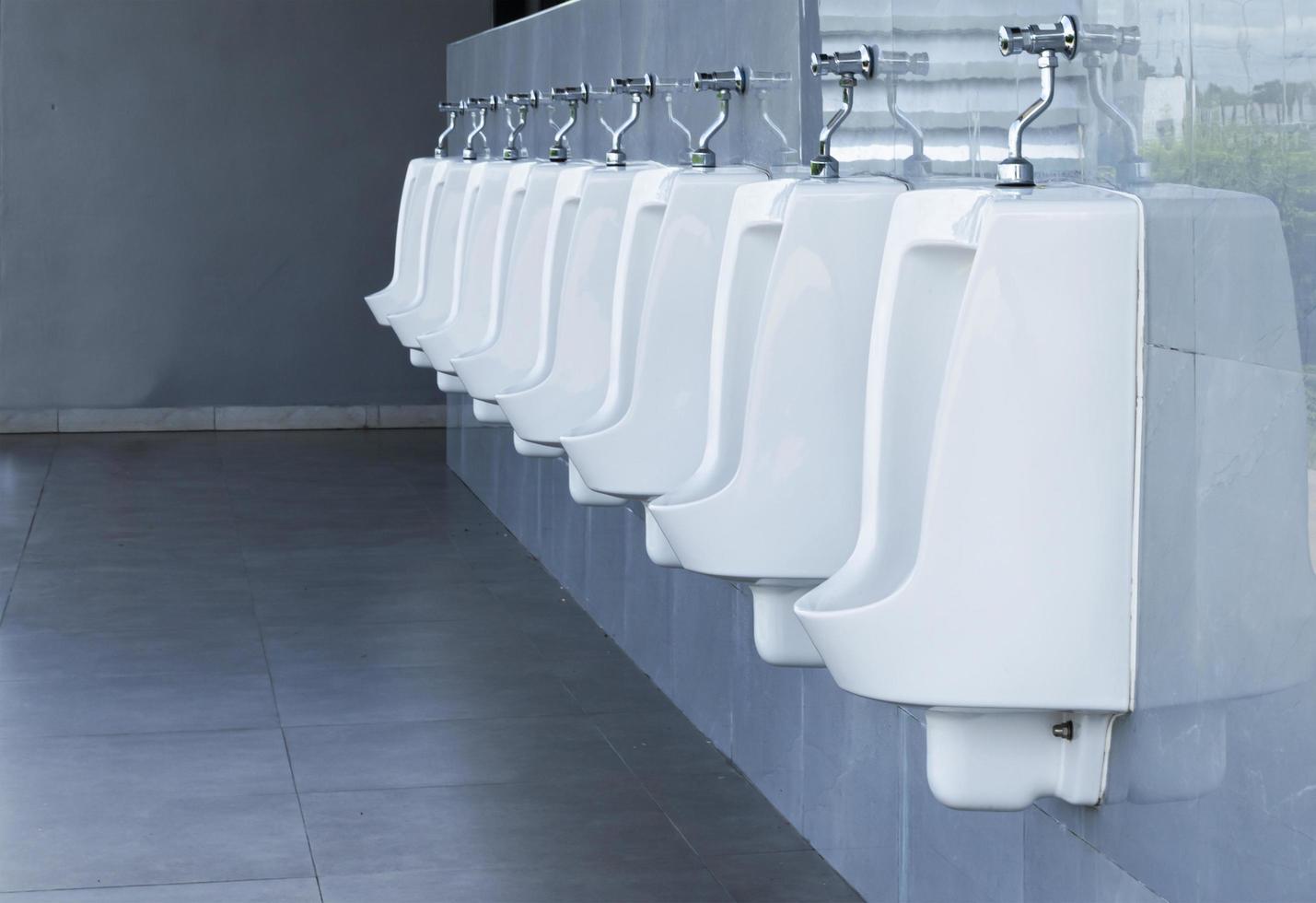 Men's room with white porcelain urinals in line in gas station photo