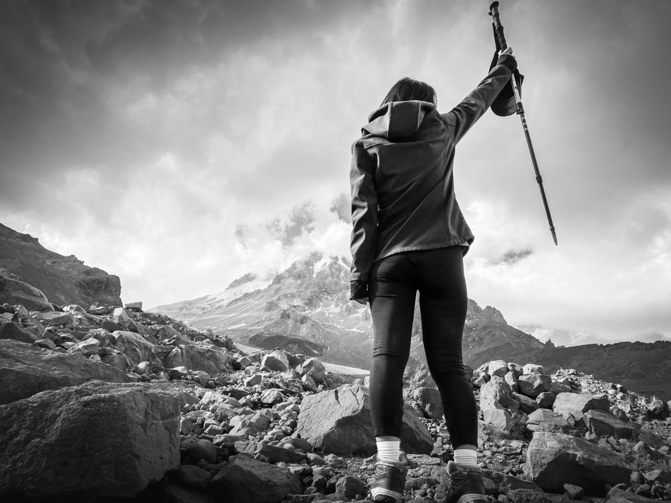 Woman hiker on rock stand on viewpoint with hands up spreaded enjoy panorama of KAzbek mountain in cloudy dramatic day photo