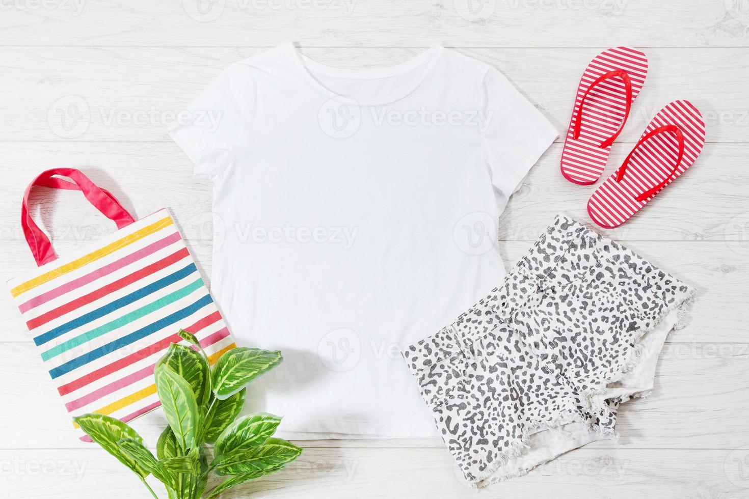 White closeup t shirt mock up flat lay and flip flops on white wooden background. Top view and copy space. Mockup summer t-shirt and summertime. Template blank shirt. photo
