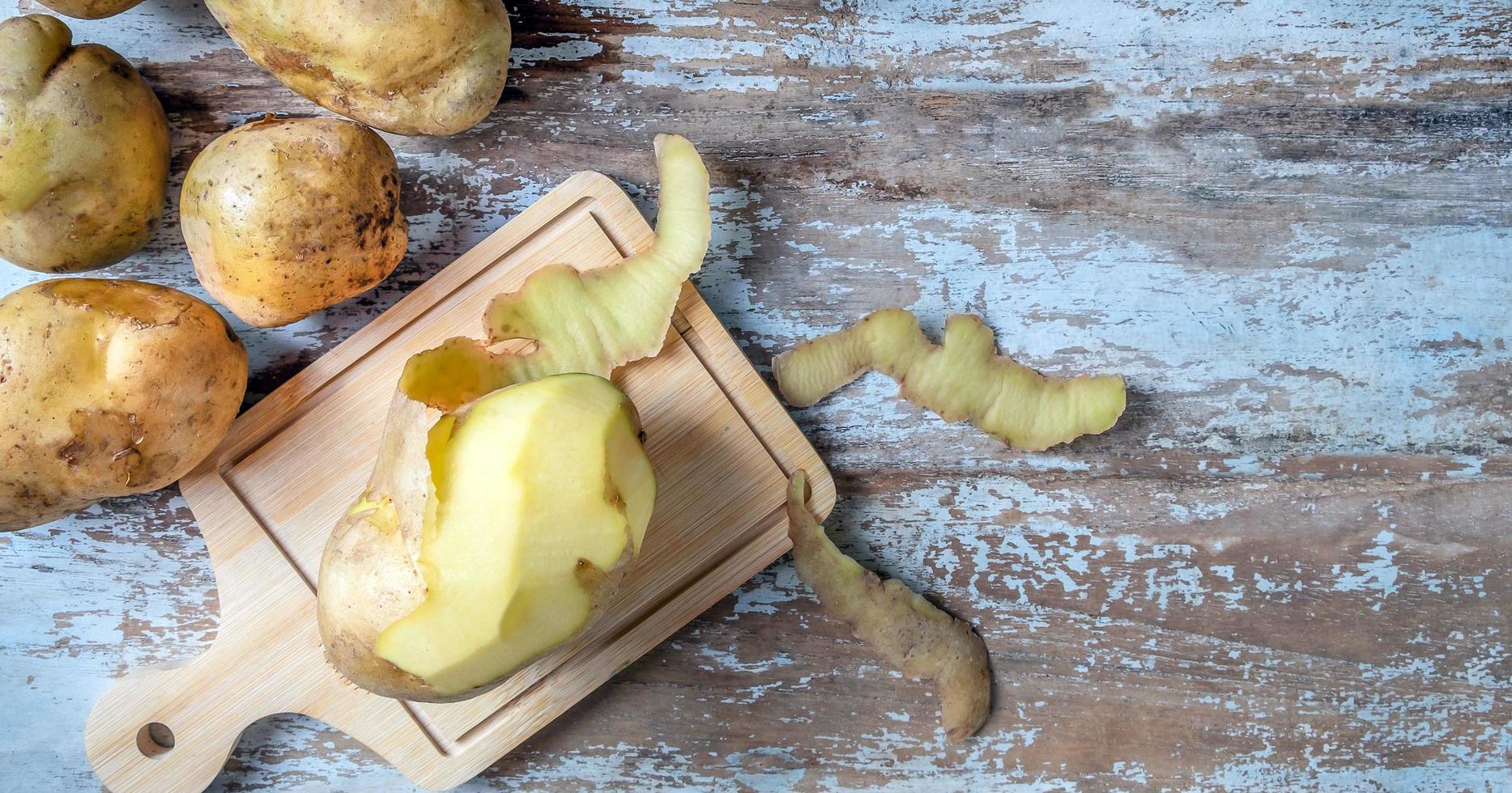 Peeled raw potatoes and raw fresh potatoes on wooden background.top view photo