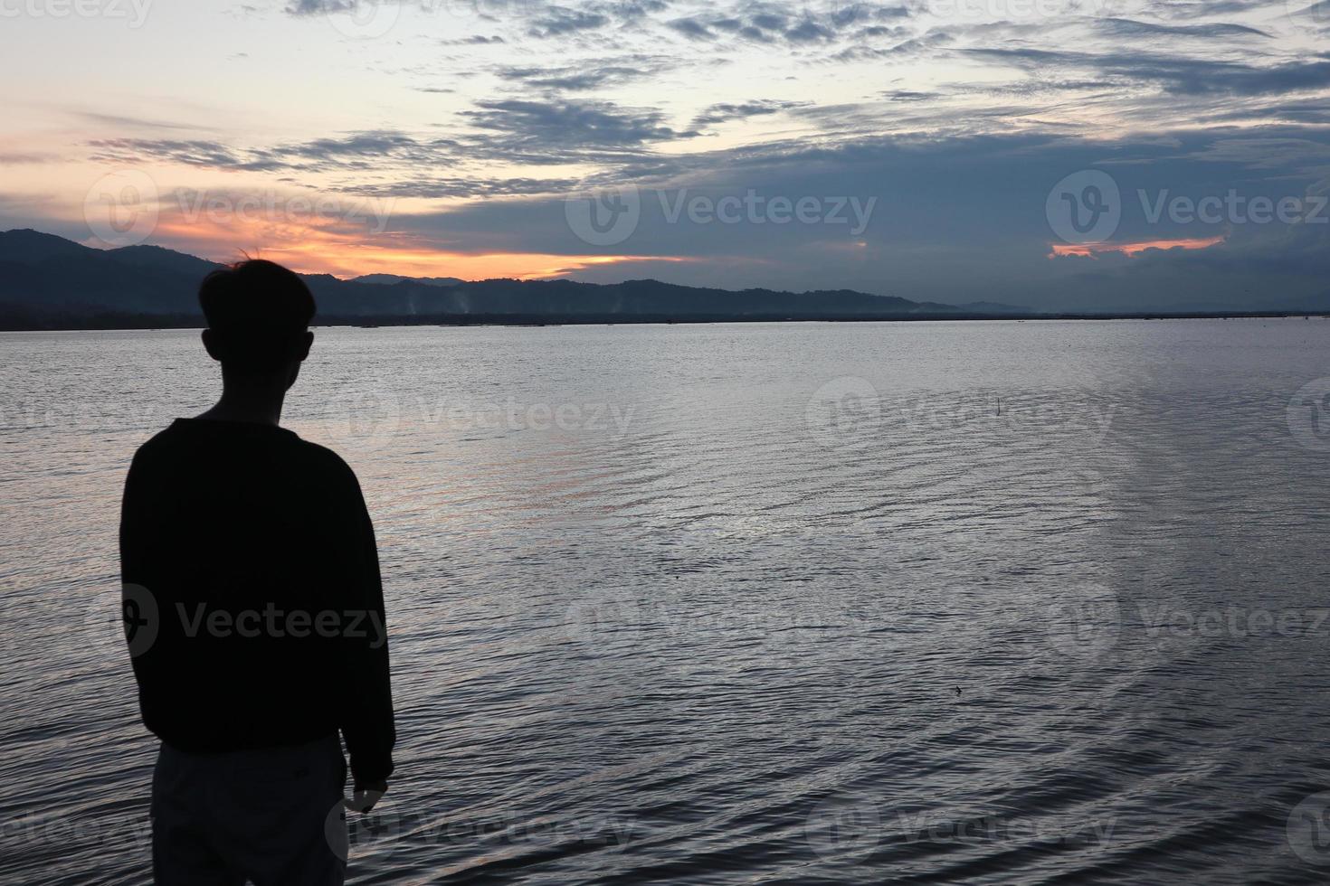 Silhouette of a young man standing by the lake enjoying the sunset. peaceful atmosphere in nature photo