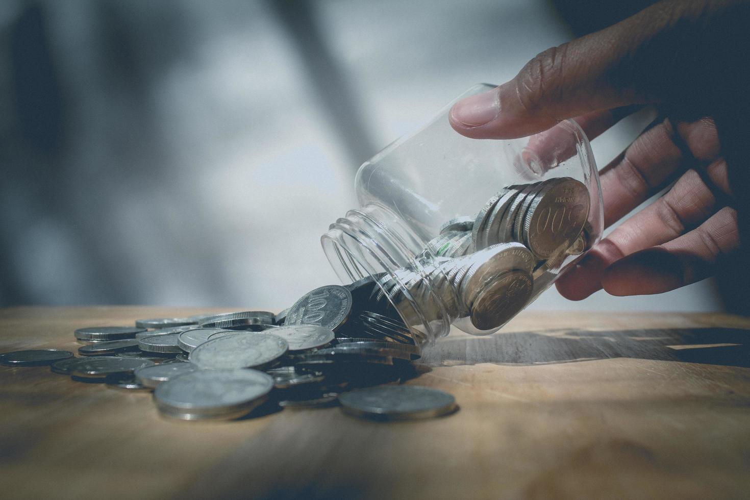 Man hand putting glass of saving coins on wooden table photo