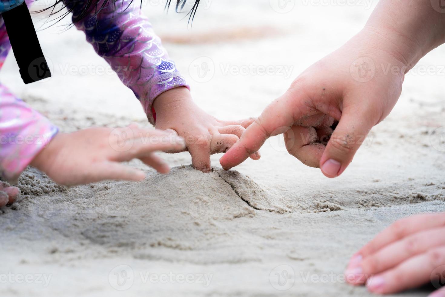 Close Up little girl's hand was drilling hole in small pile of sand she had made. Father's hand is poking at sand and playing with his daughter. Empty space for entering text. photo