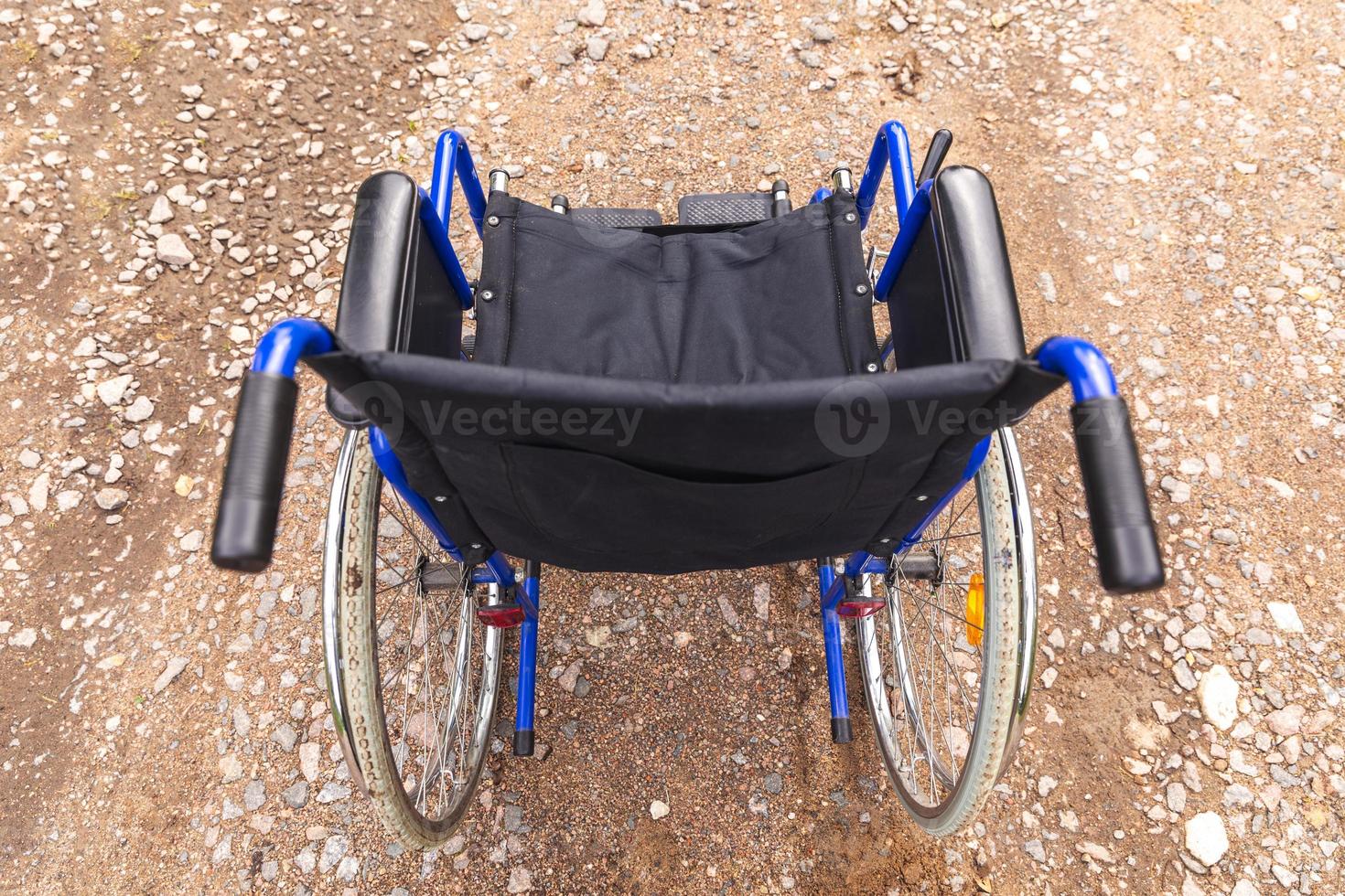 Empty wheelchair standing on road waiting for patient services. Wheel chair for people person with disability parked outdoor. Accessible for person with disability. Health care medical concept. photo