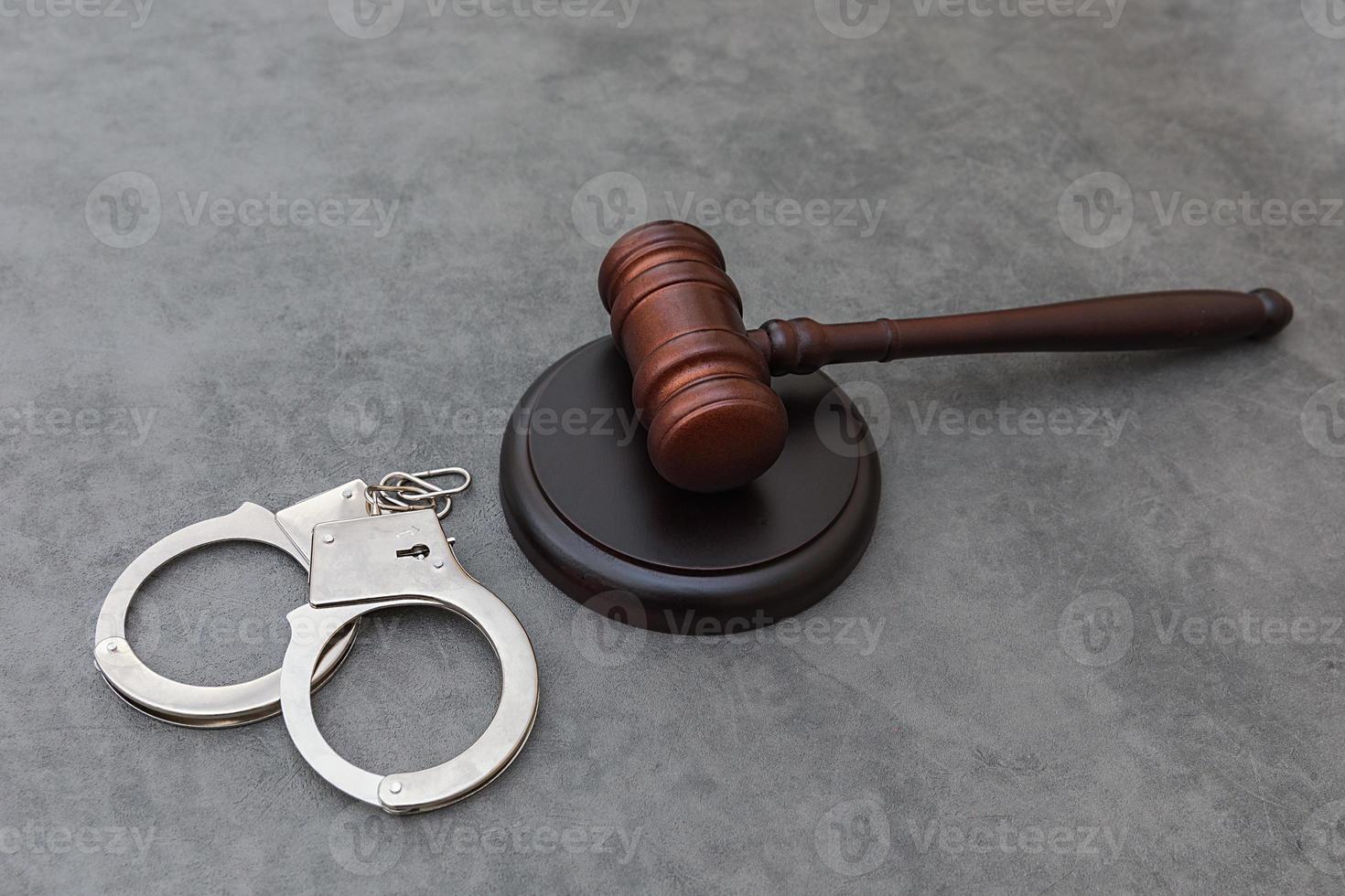 Law theme. Court of law trial in session. Judge gavel handcuffs on grey table in lawyer office or court session. Mallet of judge on concrete stone grey background. Justice human rights concept. photo
