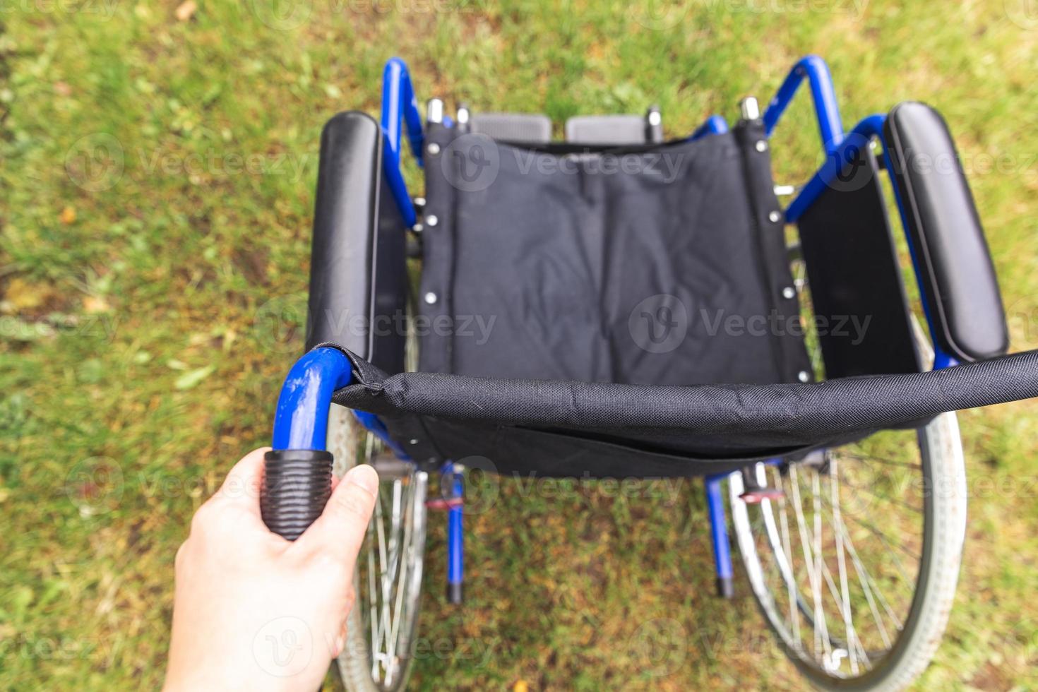 Hand holding empty wheelchair in hospital park waiting for patient services. Wheel chair for person with disability parked outdoor. Accessible for person with disability. Health care medical concept. photo