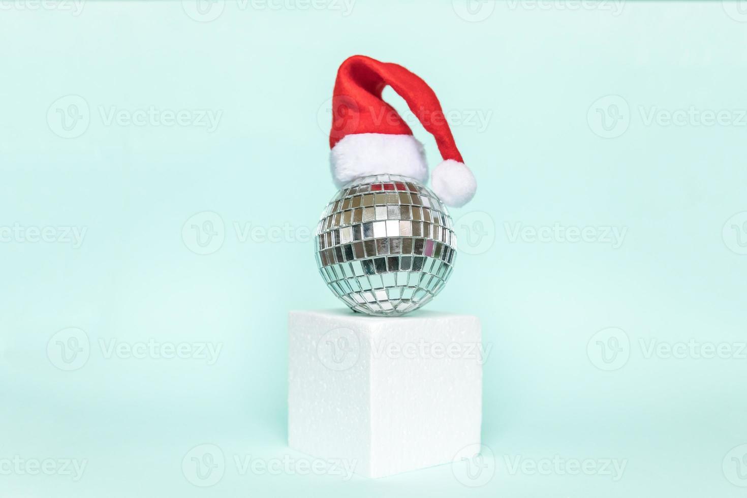 Simply minimal composition disco ball in Santa hat and cube shapes geometric form podium isolated blue pastel background. Christmas New Year december time for celebration concept. Mockup, copy space photo