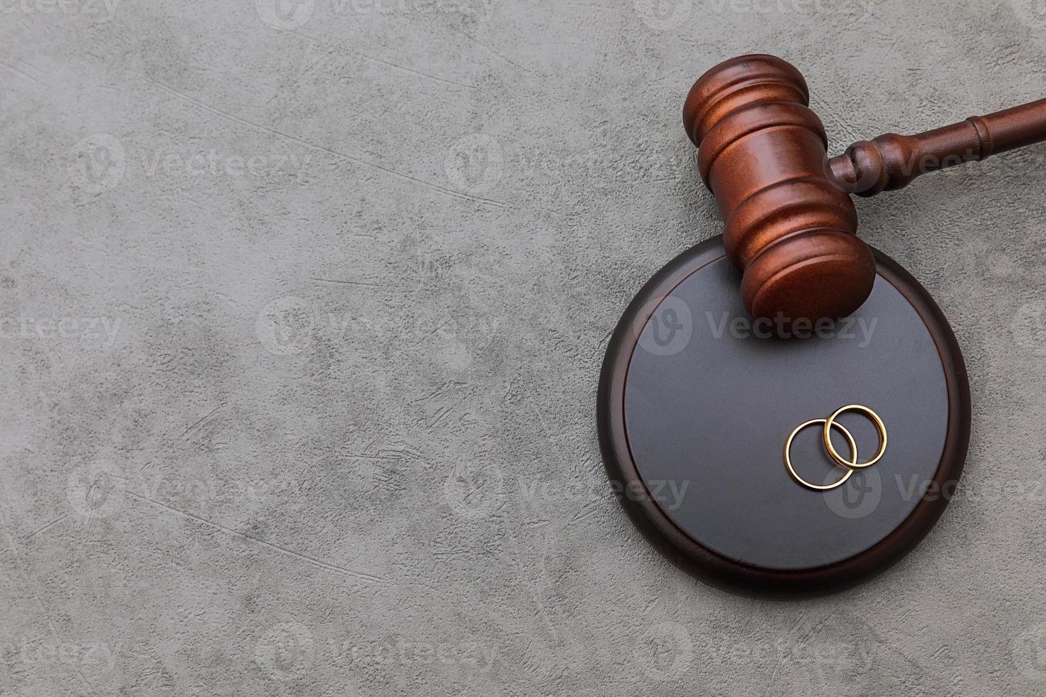 Law theme. Judge gavel wedding rings on concrete stone grey background. Divorce proceedings. Mallet of judge deciding on marriage divorce, marital agreement, legalities of divorce. photo