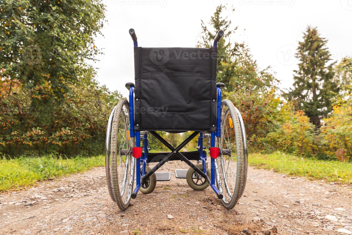 Empty wheelchair standing on road waiting for patient services. Wheel chair for people person with disability parked outdoor. Accessible for person with disability. Health care medical concept. photo