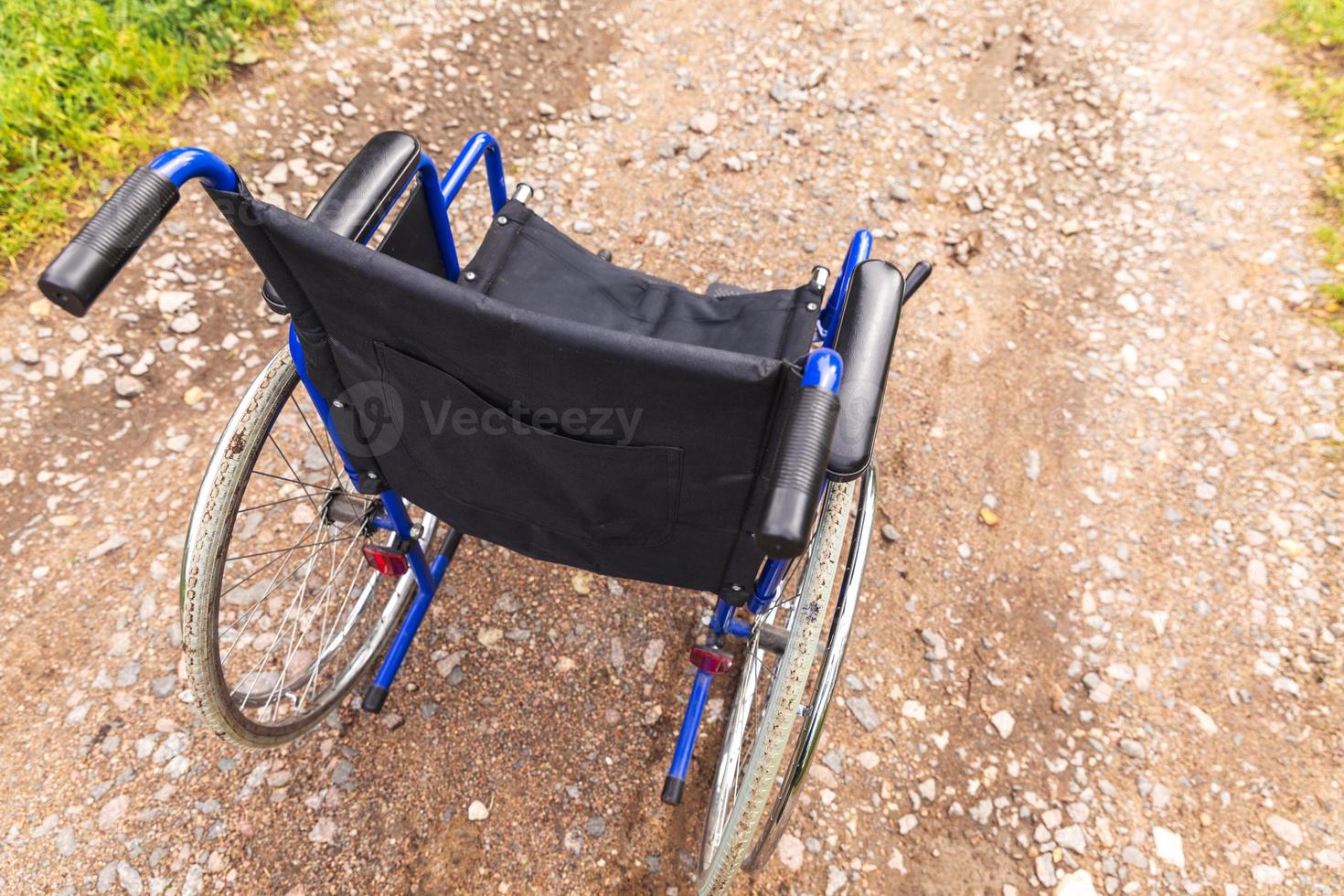 Empty wheelchair standing on road waiting for patient services. Wheel chair for people person with disability parked outdoor. Accessible for person with disability. Health care medical concept. photo