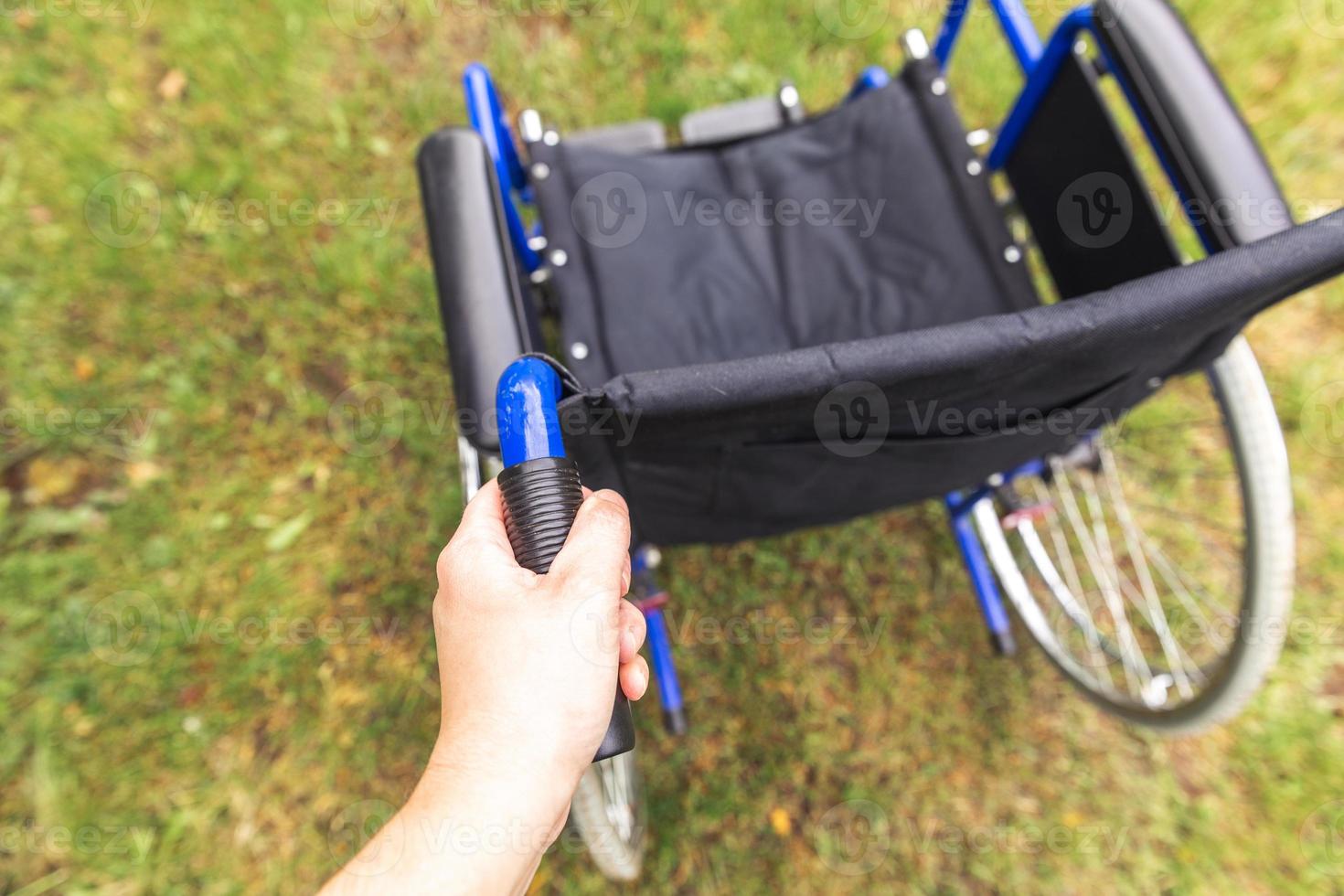 Hand holding empty wheelchair in hospital park waiting for patient services. Wheel chair for person with disability parked outdoor. Accessible for person with disability. Health care medical concept. photo