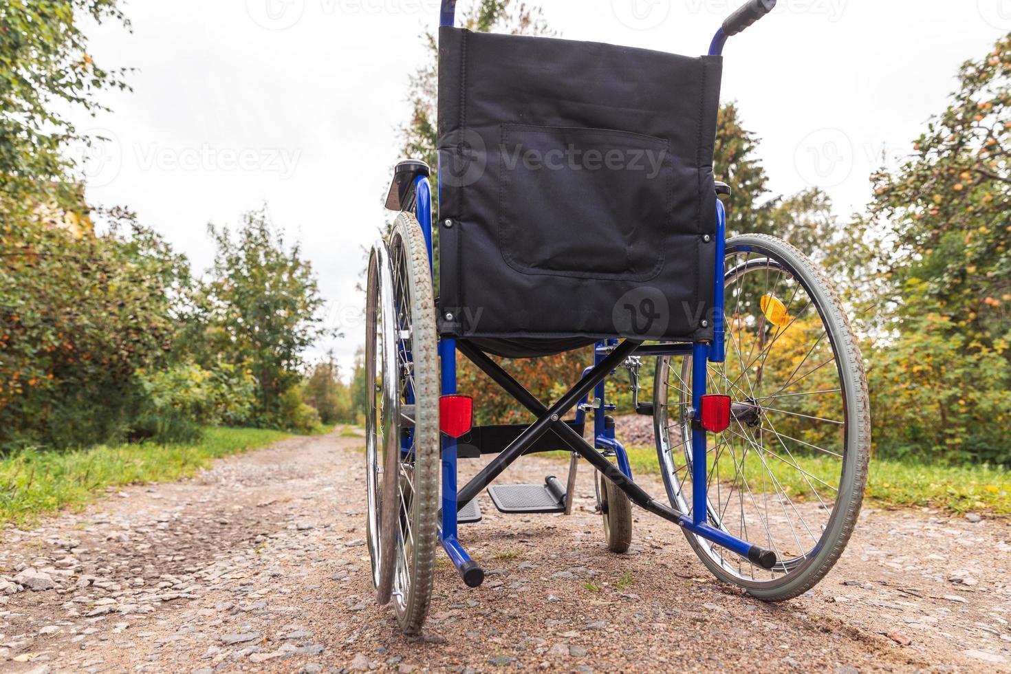 Empty wheelchair standing on road waiting for patient services. Wheel chair for people person with disability parked outdoor. Accessible for person with disability. Health care medical concept. photo