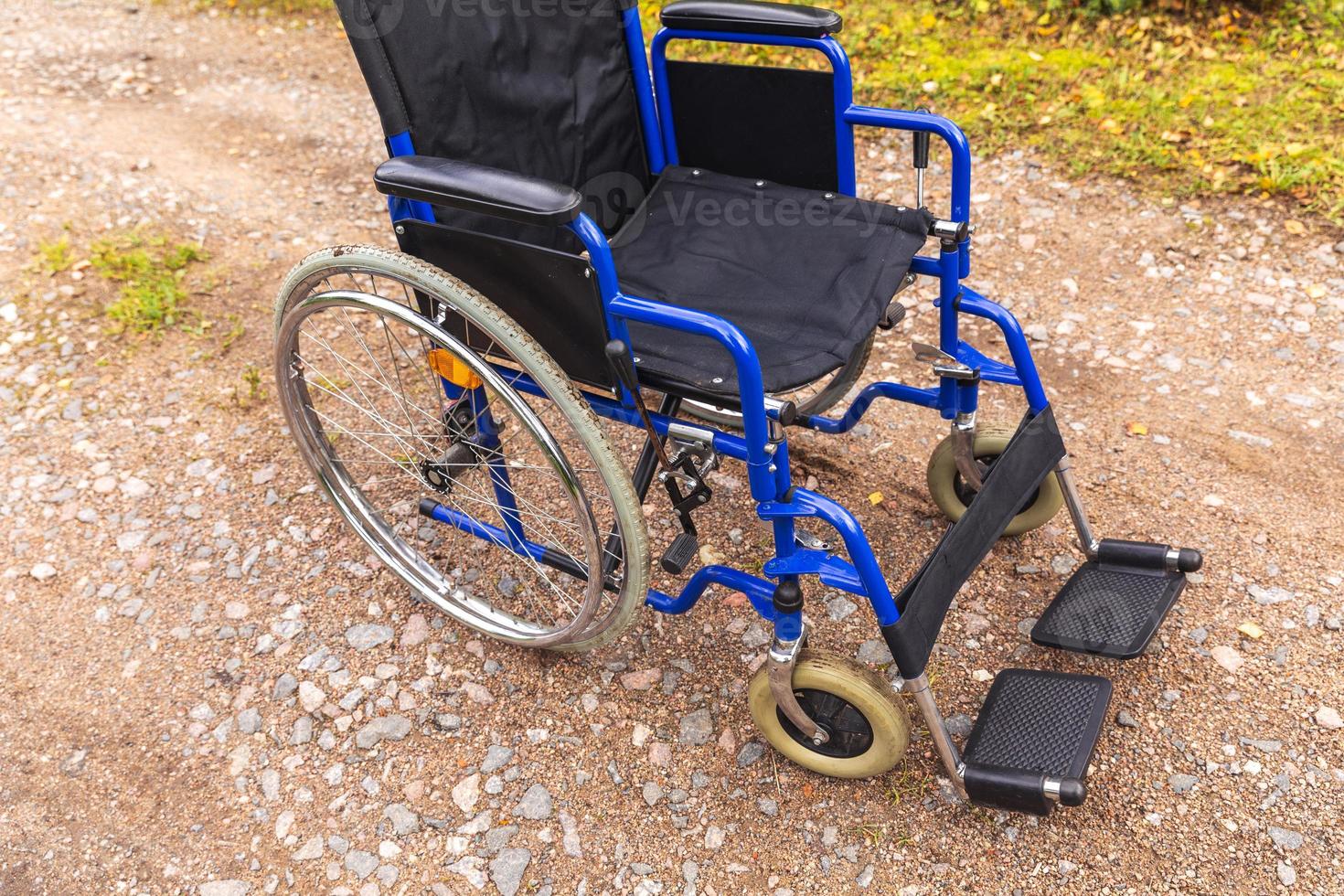 Empty wheelchair standing on road waiting for patient services. Wheel chair for people person with disability parked outdoor. Accessible for person with disability. Health care medical concept. photo