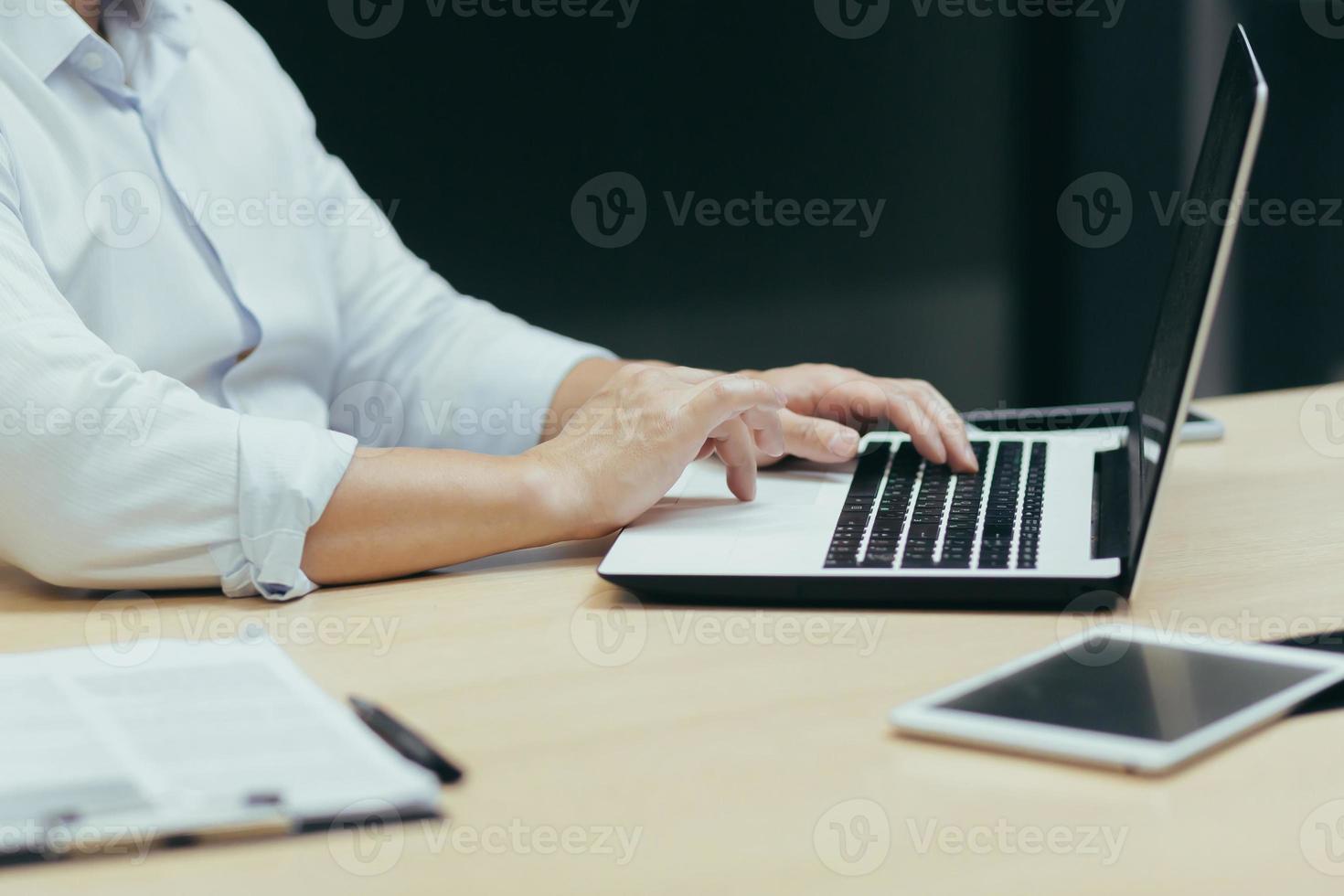 Close-up photo. Hands of a working young man behind a laptop, typing on a keyboard, in a office. photo