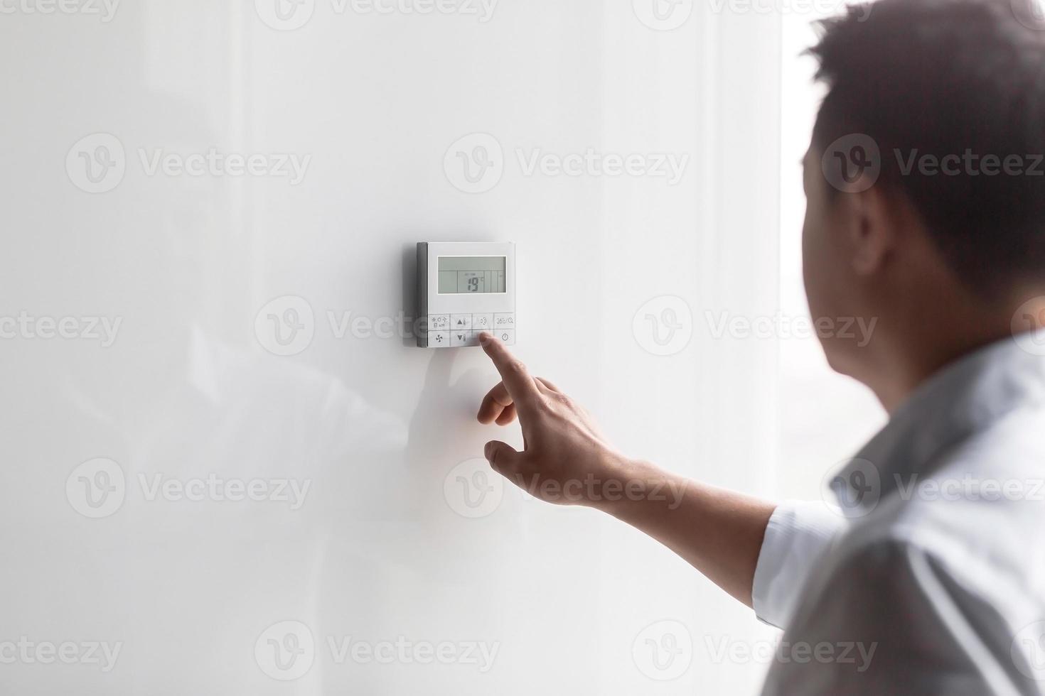 Close-up photo. The hand of a young man turns on the control buttons of the air conditioner hanging photo