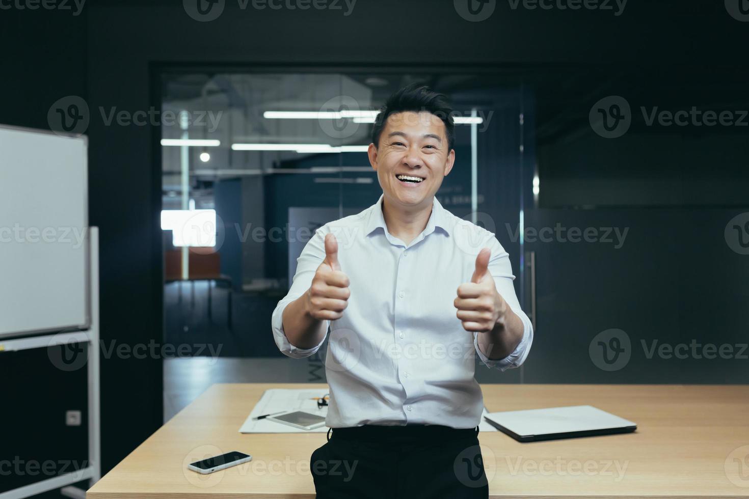 retrato del exitoso jefe de negocios asiático, hombre de pie en el cargo cerca de la mesa mirando a la cámara foto