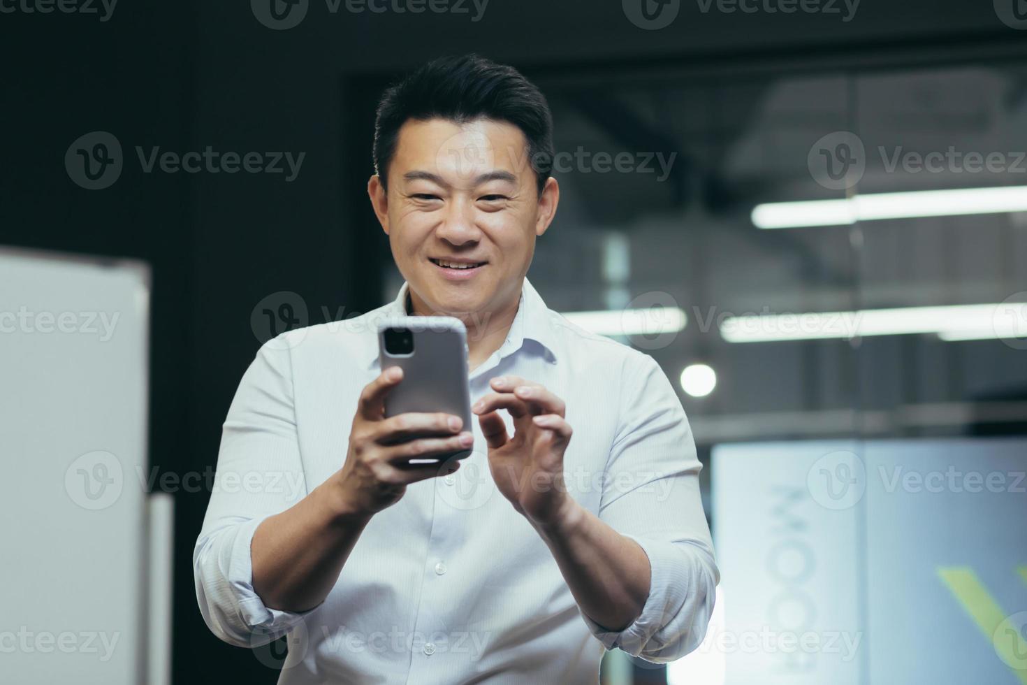 Close-up photo portrait of a male businessman in the office, standing smiling and using the phone