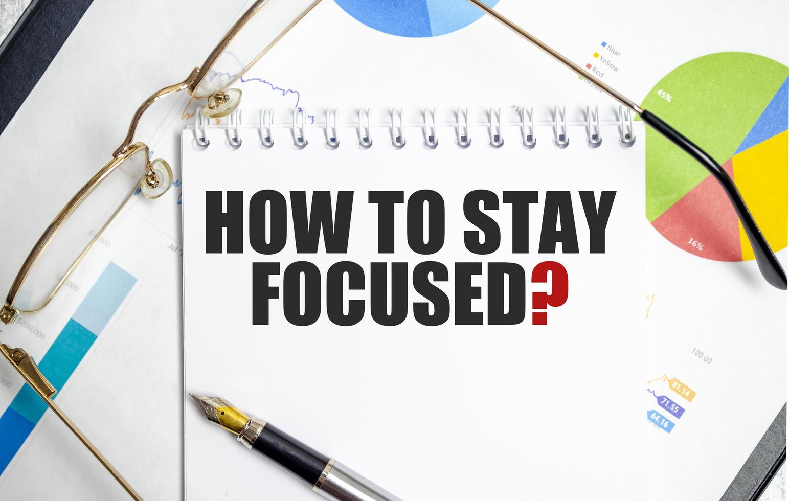 how to stay focused text written on white notebook with calculator and pen photo