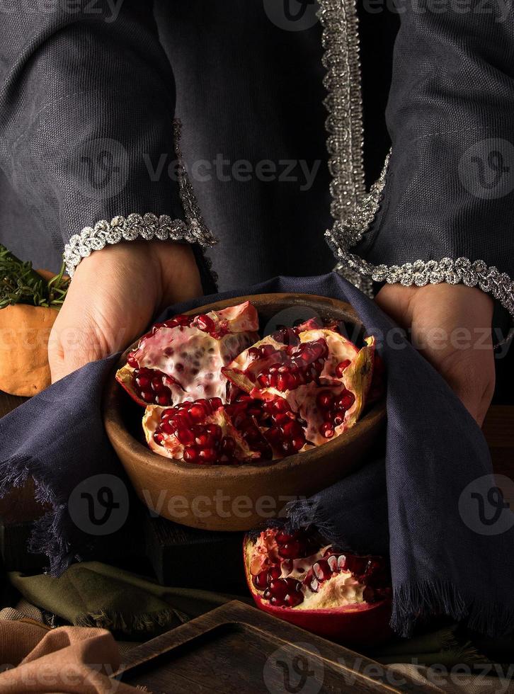 A vertical photo of woman's hands holding a bowl of pomegranate