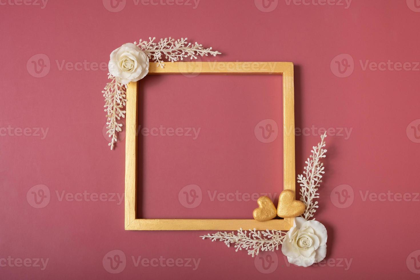 Square golden frame blank with roses and golden hearts on red background. Flat lay, top view, copy space photo