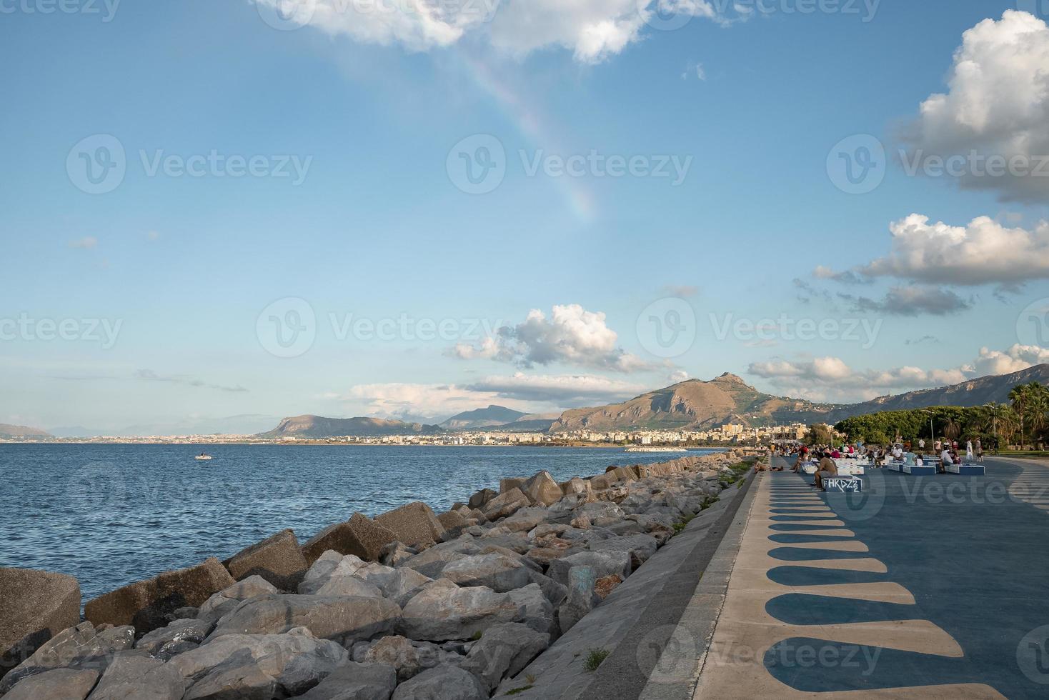 Distant view of tourists relaxing on promenade with mountains in background photo