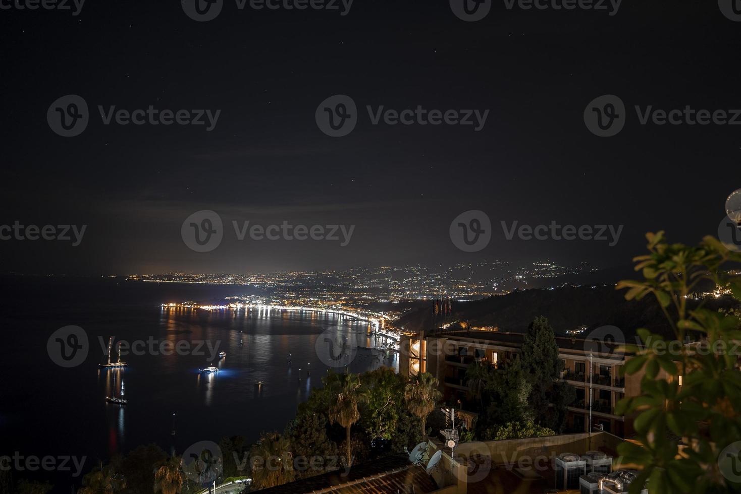Idyllic view of Hotel Elios and Mount Etna at illuminated coast by sea in night photo