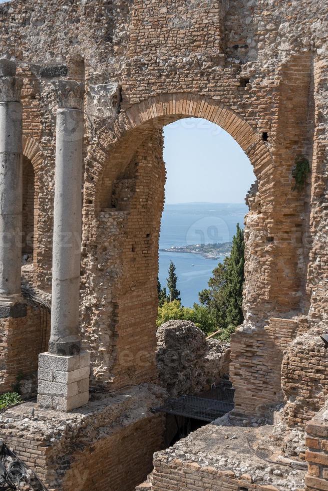Columns and arch at old ruins of ancient Greek theater with sea in background photo