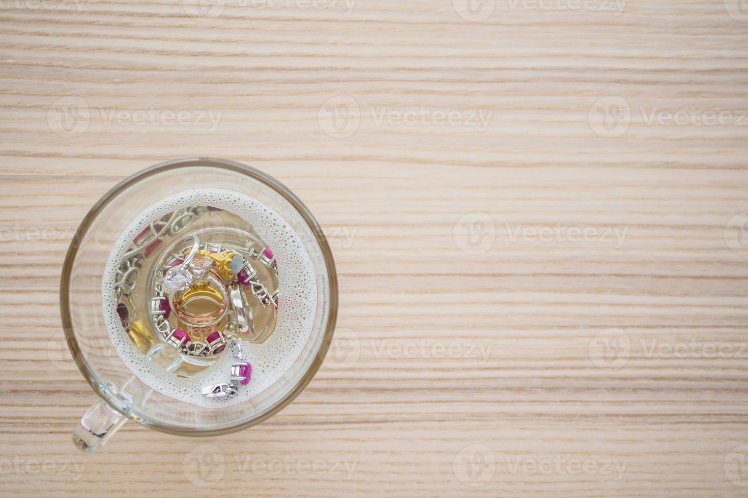 limpiar el anillo de diamantes de joyería vintage y la pulsera en vidrio sobre fondo de mesa de madera foto