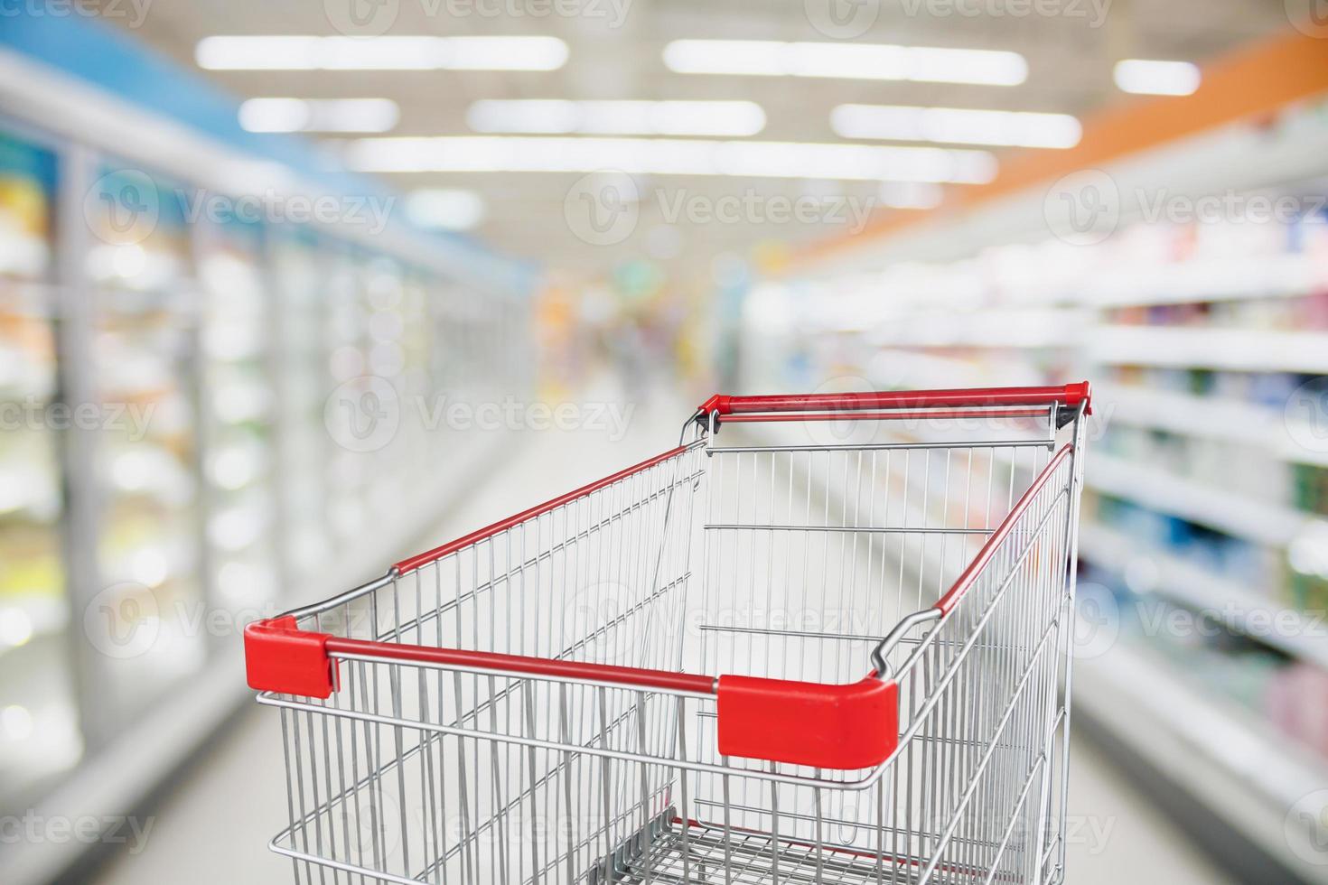 Supermarket aisle blur defocused background with empty red shopping cart photo