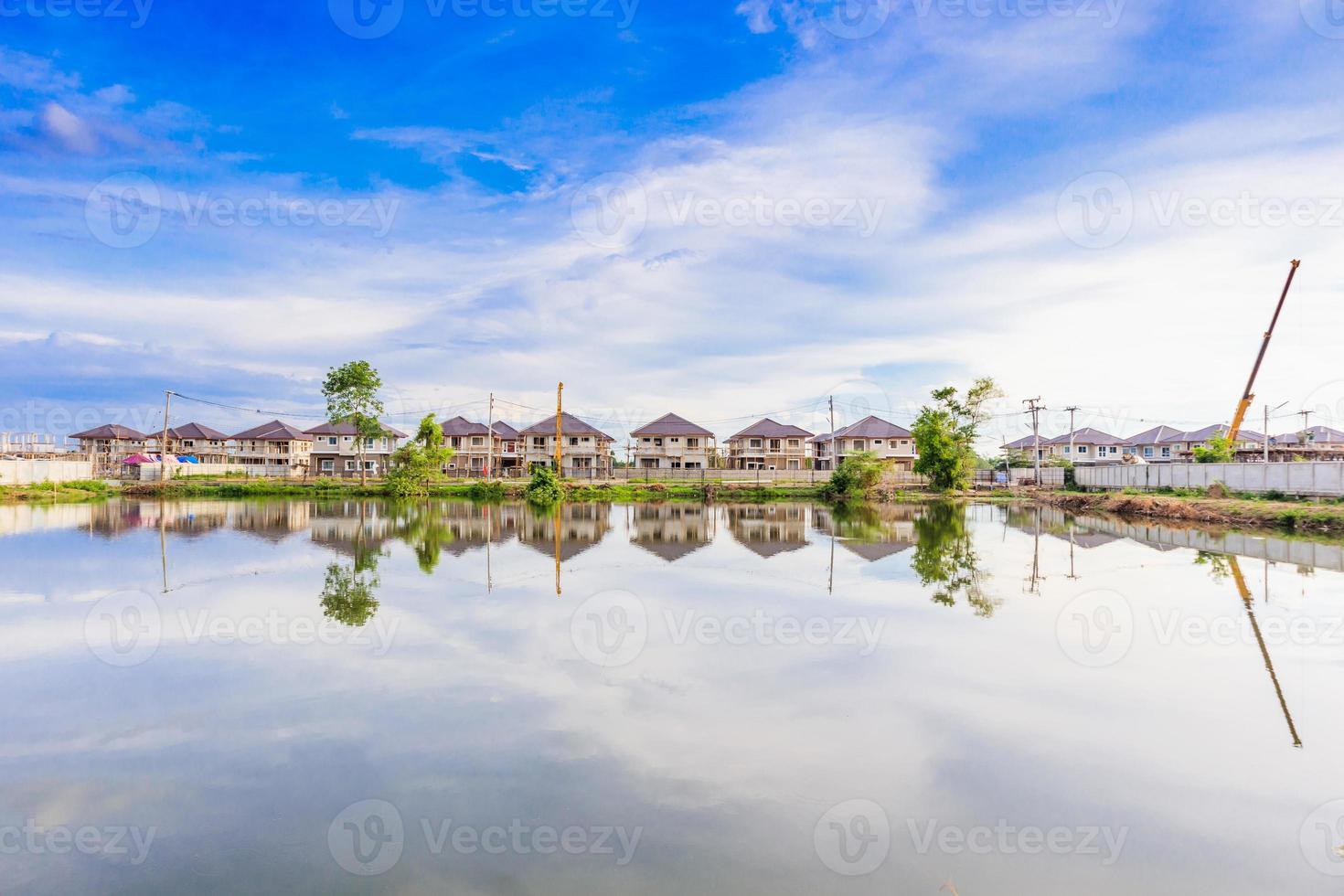 New house building reflection with water in lake at residential estate construction site with clouds and blue sky photo