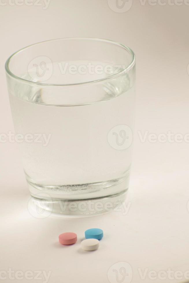 vaso de agua y pastillas sobre fondo blanco. un vaso de agua y vitaminas. estilo de vida saludable, suplementos nutricionales. foto
