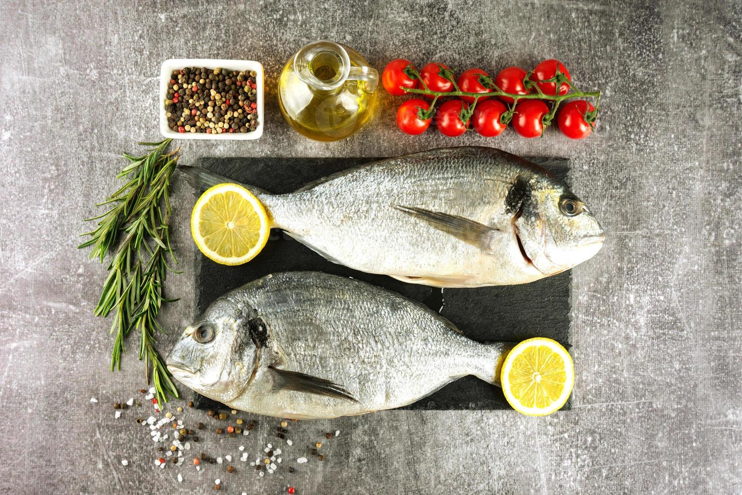 Fresh fish dorado on black slate cutting board and grey concrete background with ingredients for cooking photo