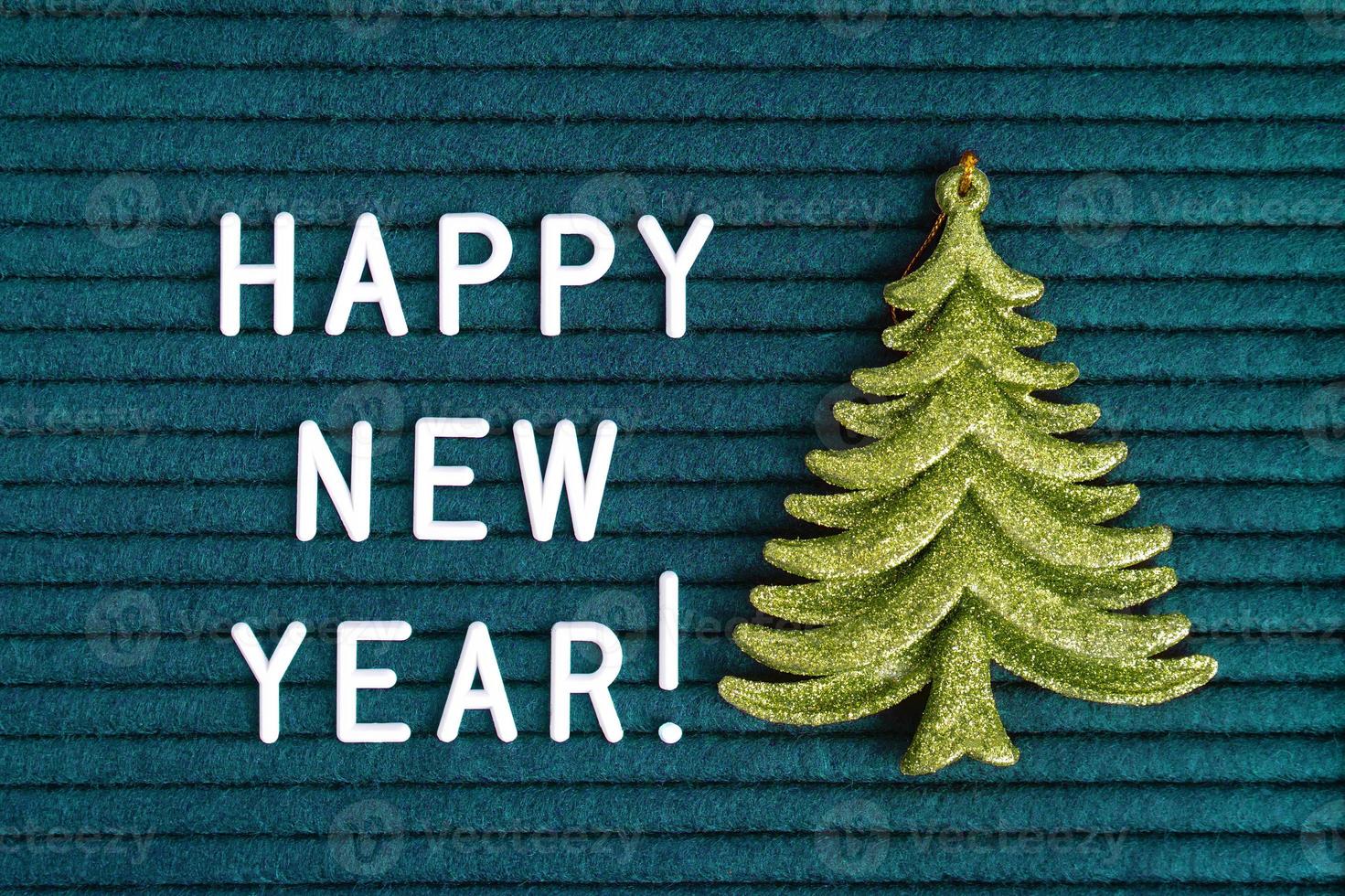 Happy new year , text on dark turquoise felt letter board with white letters and green toy fir photo