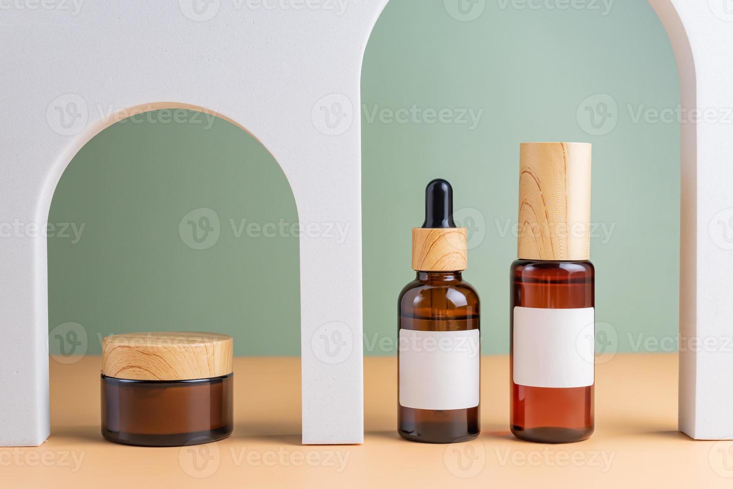 A mock-up of a brown cosmetics bottles with dispenser and white label and bottle with pipette in white arched doors for cosmetics photography on beige colored background photo