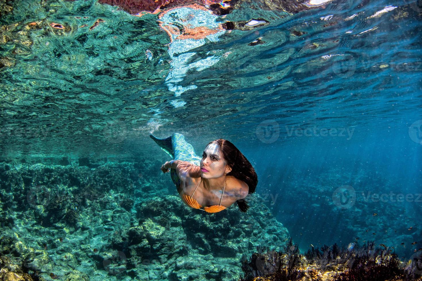 Mermaid swimming underwater in the deep blue sea photo
