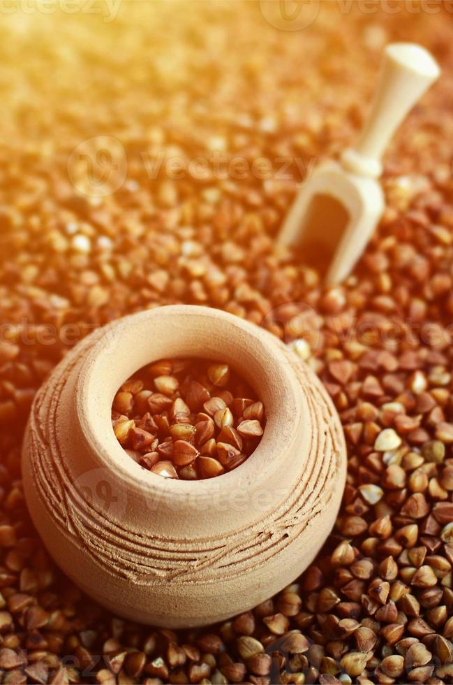Background image of a large pile of buckwheat, in the middle of which lies a small jug and a wooden spatula for cereals photo