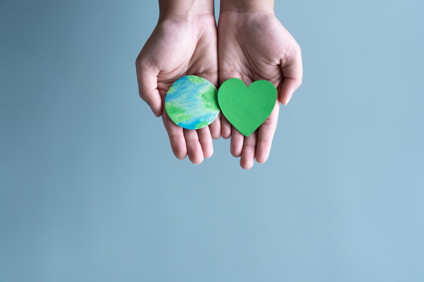 Hands holding earth and green heart shape. Concept of protecting the world from global warming with eco-heart in mind. photo