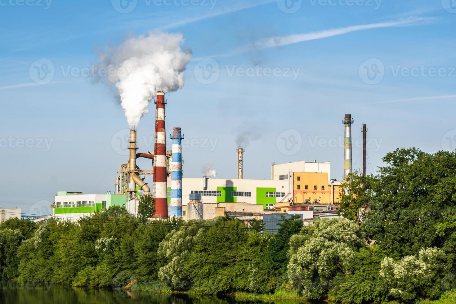 tuberías de aserradero de planta empresarial de carpintería con un hermoso reflejo en el agua azul del río. concepto de contaminación del aire. paisaje industrial contaminación ambiental residuos de central térmica foto