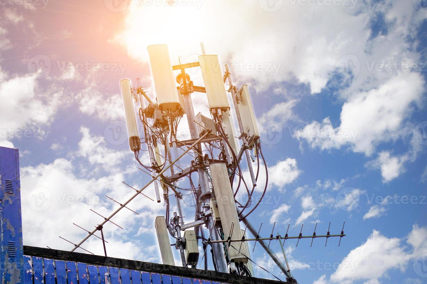 Communication tower with antennas on the top of building and bright blue sky with sun flare and big clouds background. photo