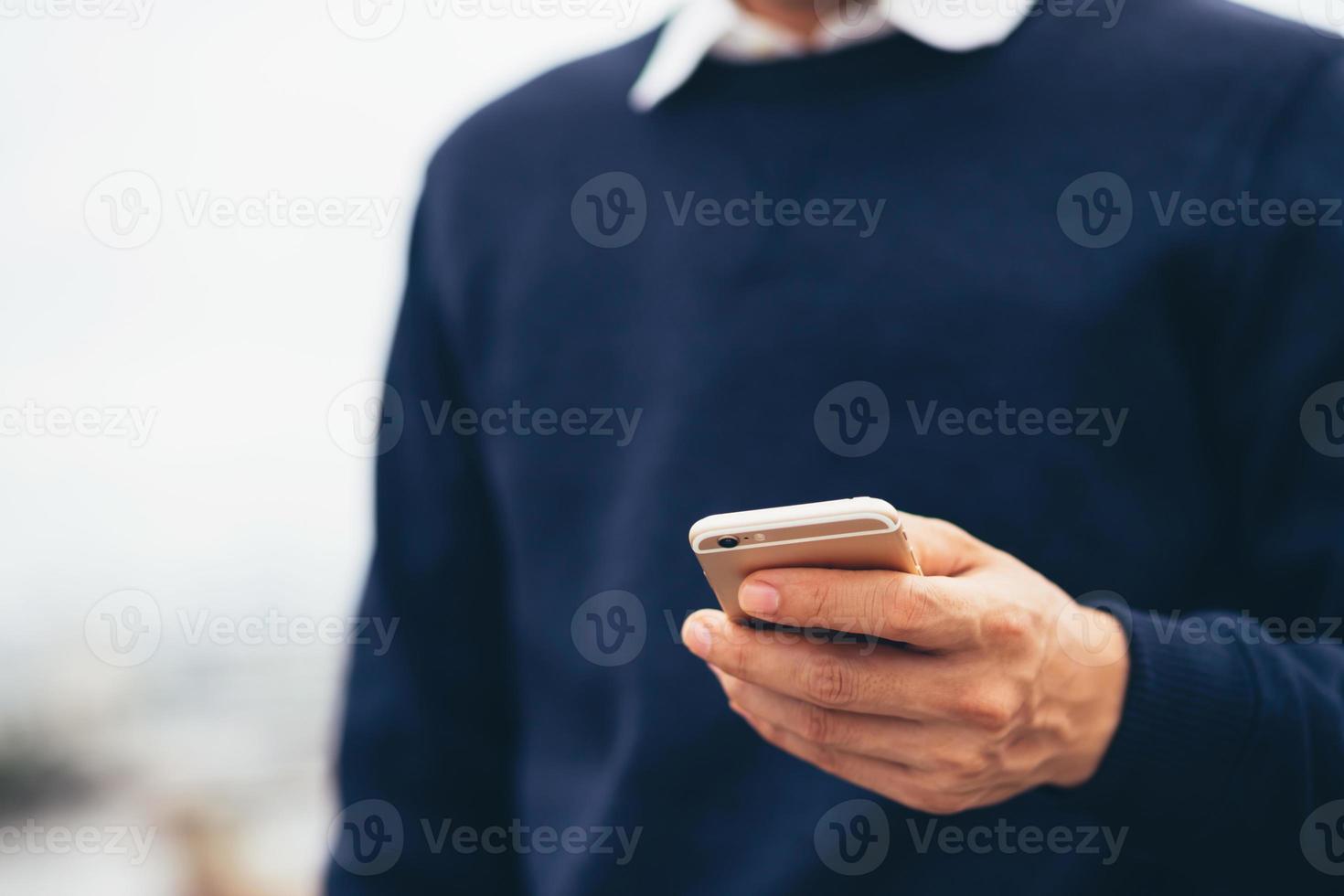 joven usa camisa a cuadros. cierre la mano usando el teléfono celular durante el descanso en el sofá. sentado viendo un mensaje en un teléfono inteligente móvil durante el descanso, relájese. enfoque suave. foto