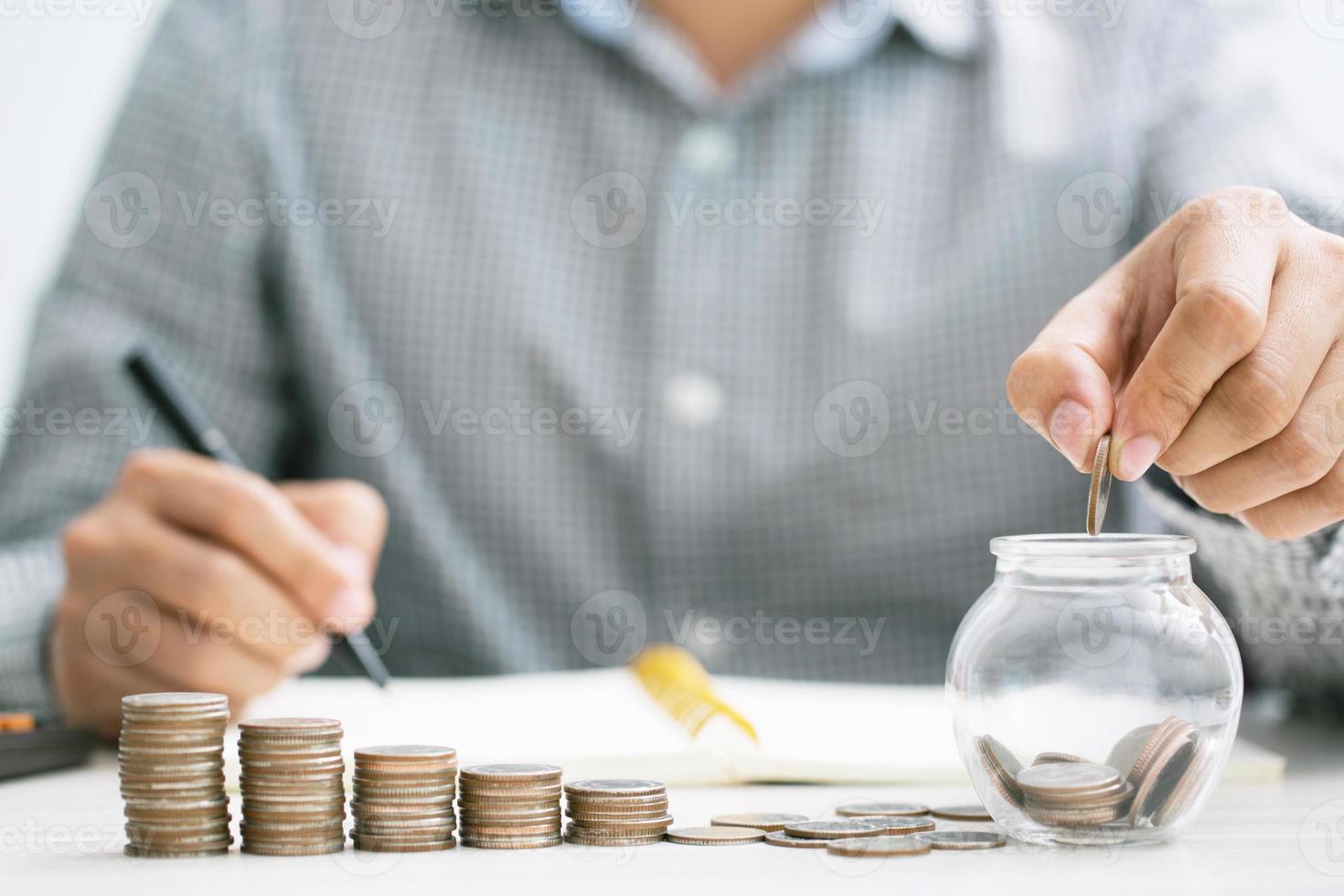 close up hand business man accounting calculator with savings money coins stacked row with hand putting coins in jug glass. concept Write Finance accounting. photo