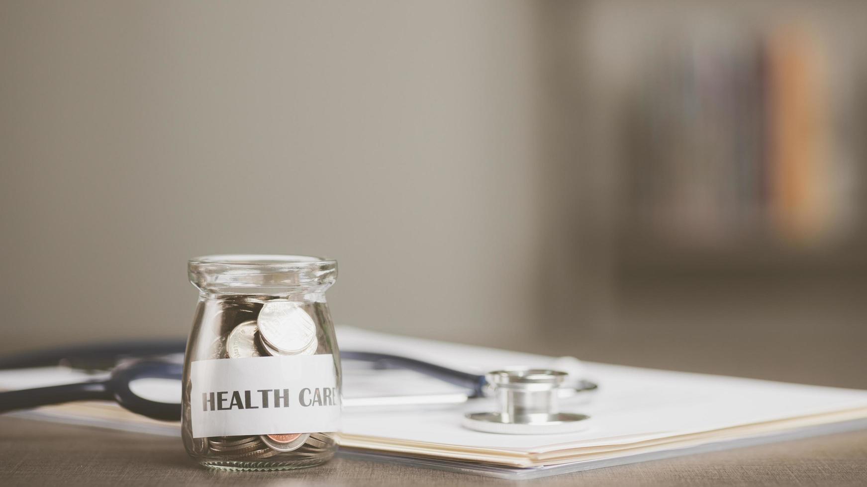 message on paper and coins in glass jar, stethoscope and medical report, all on table, savings concept, for health care expenses, financial health check, control financial risks, insurance investments photo