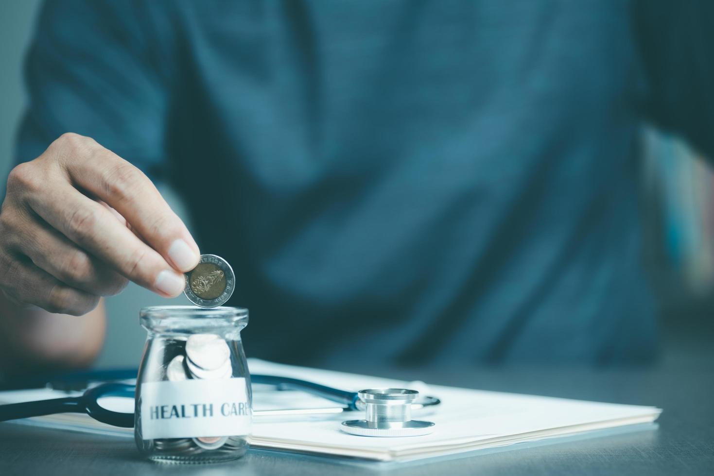 young man put the coin in the jar, the stethoscope and the medical report. all on the table Savings concept, for medical expenses, financial health check, financial risk control, insurance investment photo