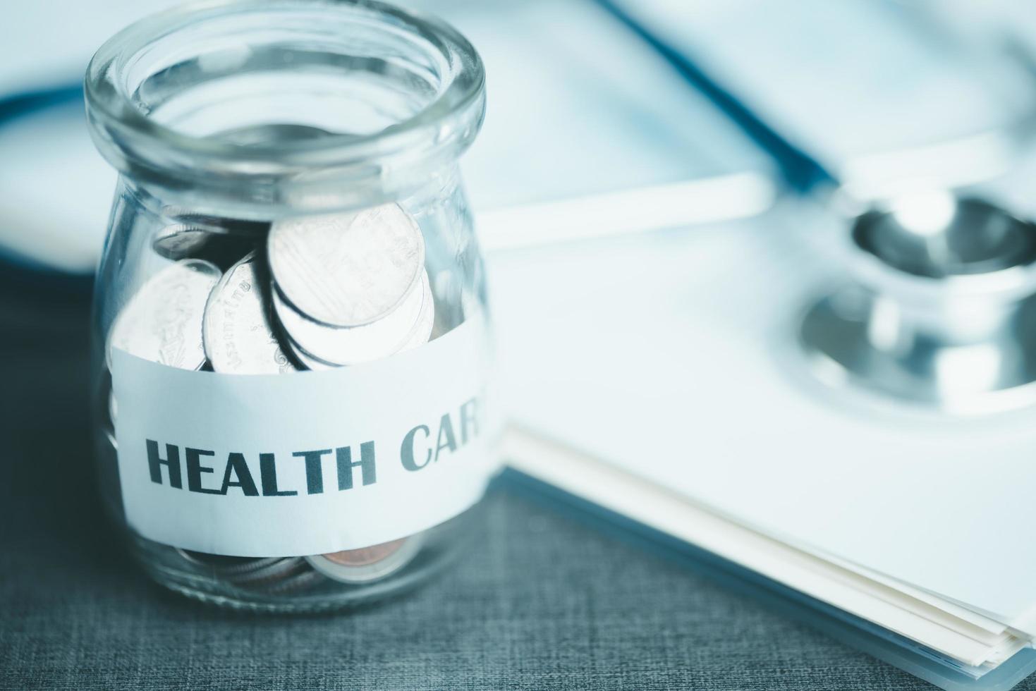 message on paper and coins in glass jar, stethoscope and medical report, all on table, savings concept, for health care expenses, financial health check, control financial risks, insurance investments photo