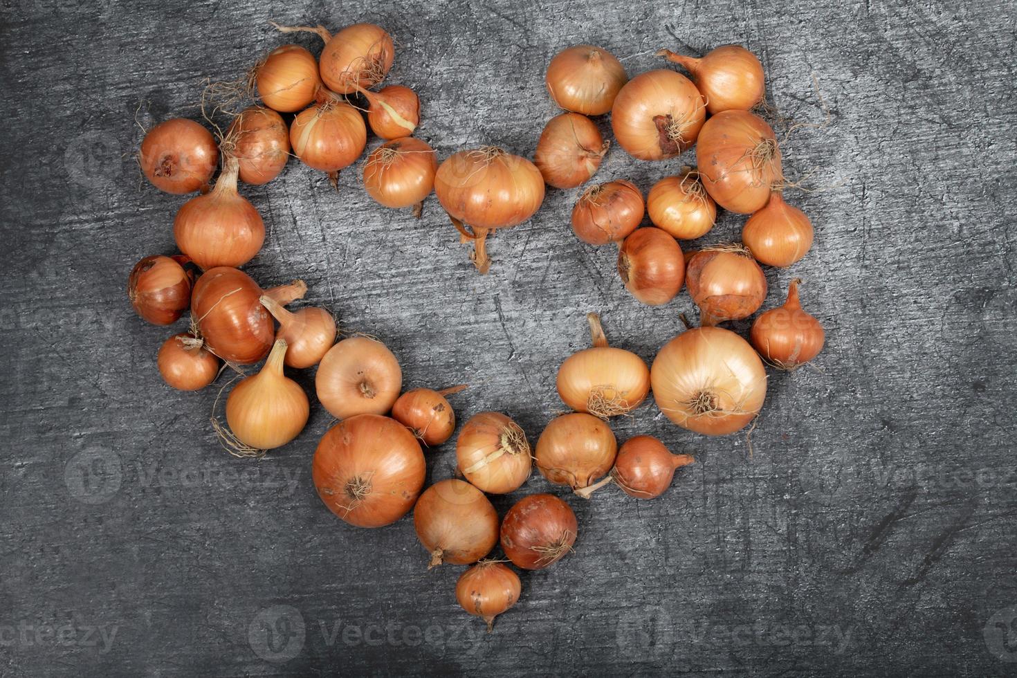 Many brown onions lie next to each other on a light gray background and form a heart photo
